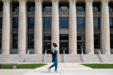A student walking along State Street in front of the eight Doric columns that surround the entrance to Angell Hall.