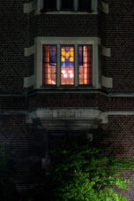 A University of Michigan flag shines through a window of the Martha Cook Building.