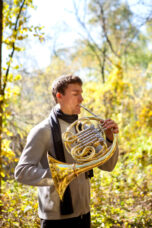 A music student uses the natural acoustics in the woods to practice his french horn on North Campus.