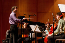 A graduate student directs the orchestra for a Composers Forum in Britton Recital Hall.